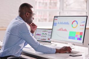 Man analysing data on multiple screens, showing the benefits of automating payroll for enhanced reporting and analytics.