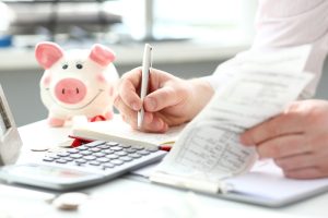 A person calculating expenses with a calculator and receipts, with a piggy bank on the desk, representing cash flow management.