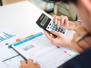 Hands calculating tax penalties using financial documents, graphs, and a calculator, representing small business financial management.