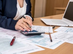 Businesswoman calculating tax strategy with paperwork and a calculator on the desk.